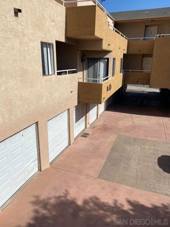 Outdoor parking area with multiple garage units beneath a building.