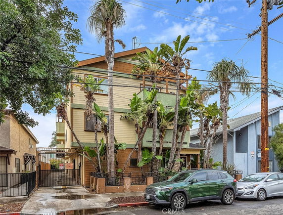 Front view of a multi-story residential building with palm trees and parked cars.