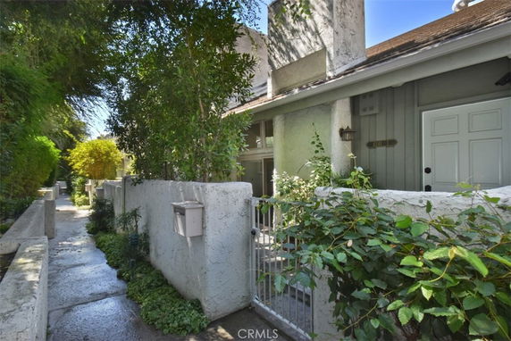 Front view of a house with a gated entrance and exterior walls partially covered with plants.