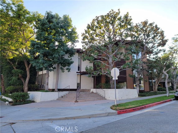Front view of a multi-story building with large trees and a staircase leading to the entrance.