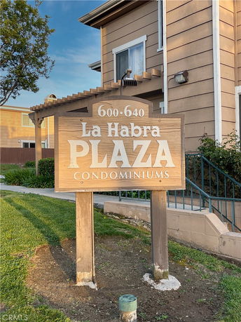 Front view of a condominium building with a wooden sign stating 'La Habra Plaza Condominiums'.