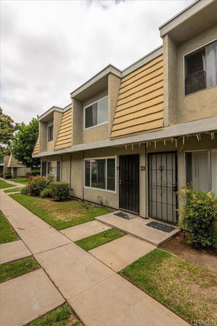 Front view of a two-story apartment building with a concrete walkway and small lawns.