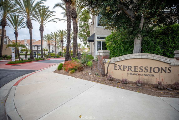 Entrance to a residential complex with a sign reading 'Expressions at Rancho Niguel' and palm trees lining the road.