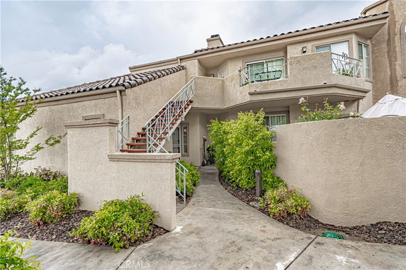 Front view of a beige two-story house with a staircase leading to the upper level and a balcony.