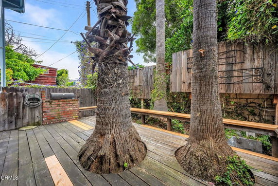 Wooden deck area with large tree trunks and a brick outdoor grill.