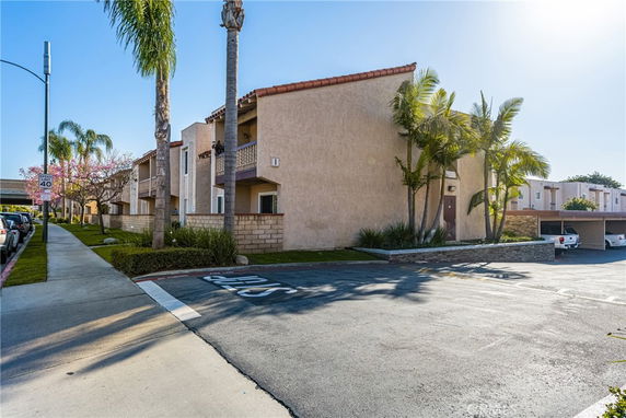 Front view of a multi-story apartment building with balconies and surrounding palm trees.