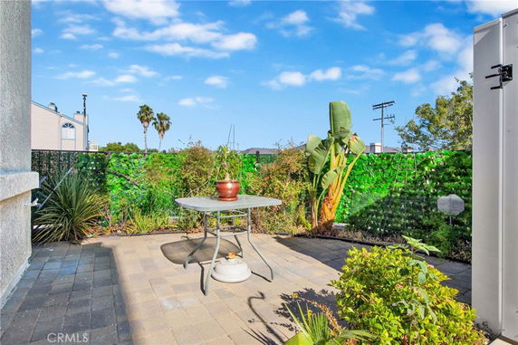 Outdoor patio area with a table and plants, surrounded by greenery and distant view of buildings.