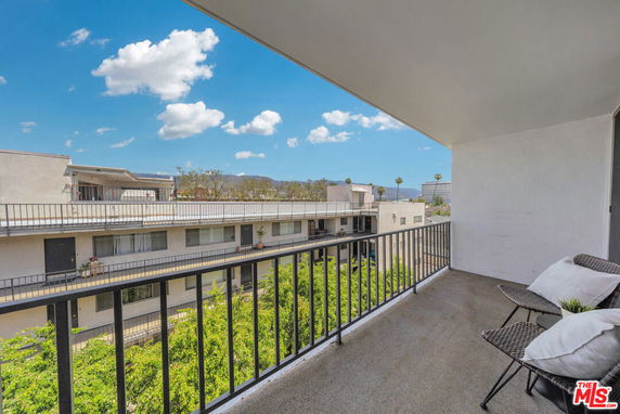 Balcony view showing surrounding buildings and distant hills under a clear blue sky.