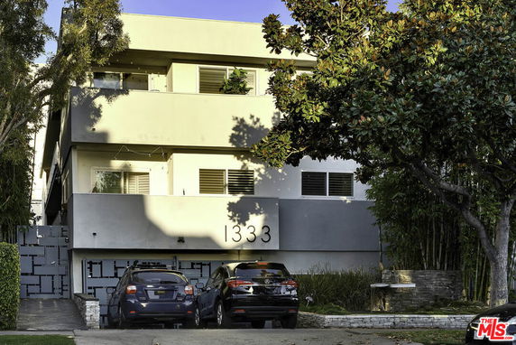 Front view of a multi-story residential building with two parked cars.