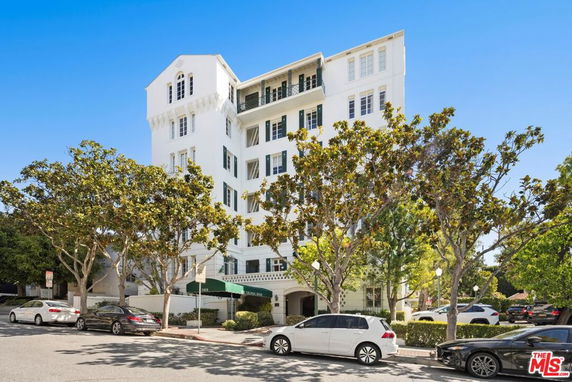 Front view of a multi-story white building with balconies and large windows.