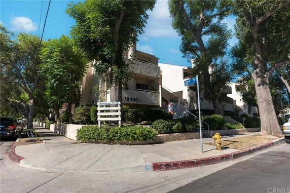 Front view of a multi-story building with a sign and trees surrounding it.