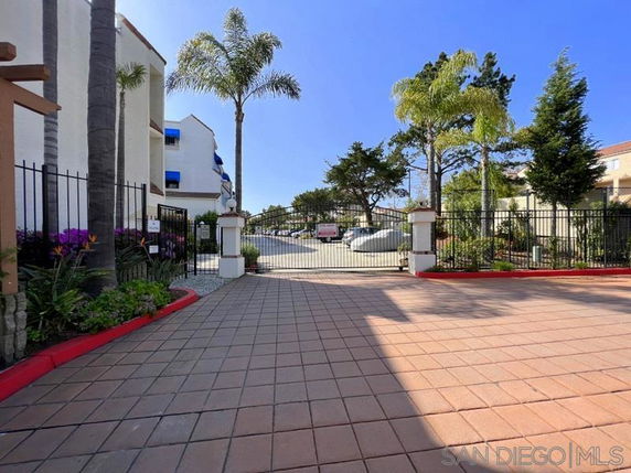 Entrance view of an outdoor parking area with a gated entry and surrounding buildings.