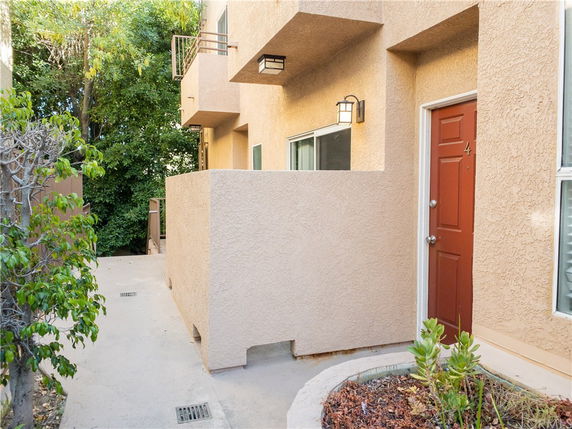 Front view of a building entrance with a red door and a small patio area.