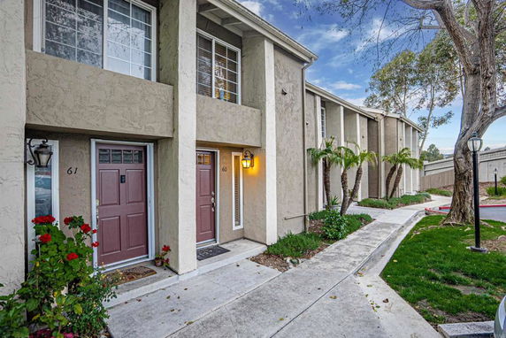Front view of a multi-story townhouse with a concrete path and numbered doors.