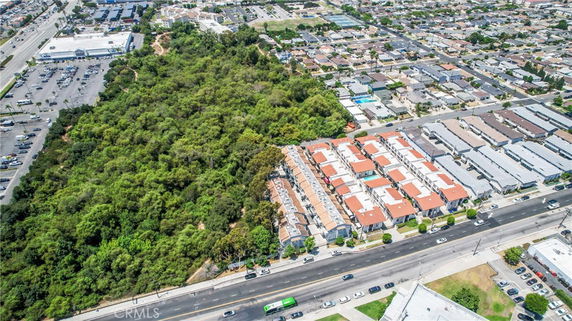 Aerial view of residential buildings adjacent to a forested area and a commercial district.