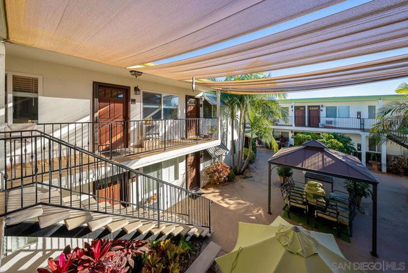 Exterior courtyard view of a multi-level apartment complex with doors and windows, covered seating areas, and plants.
