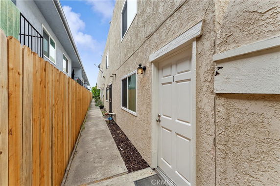 Exterior view of a narrow walkway between two buildings with a wooden fence on one side.