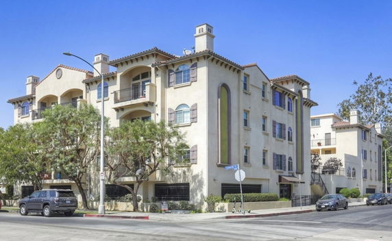 Front view of a multi-story apartment building with balconies and a tiled roof.