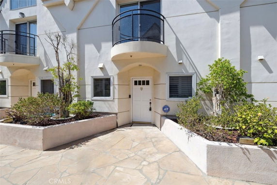 Front view of a multi-story building with a white exterior, balcony, and entrance.