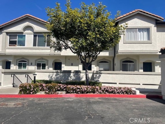 Front view of a two-story residential building with a tree and shrubs.