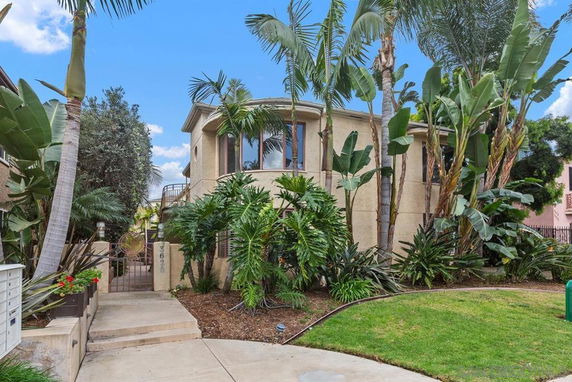 Front view of a two-story house with decorative plants and trees in the front yard.