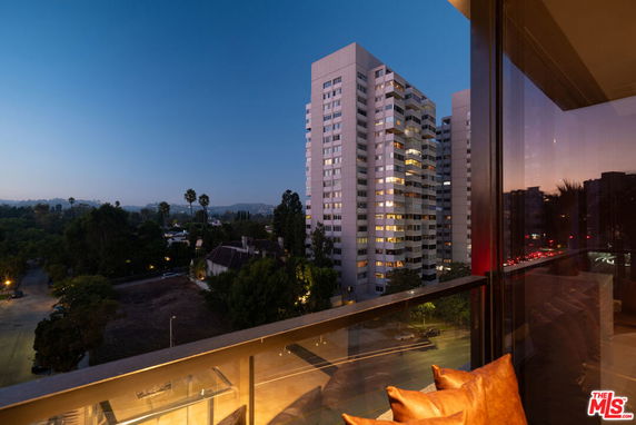 Evening view from a balcony overlooking a cityscape with tall buildings and surrounding greenery.