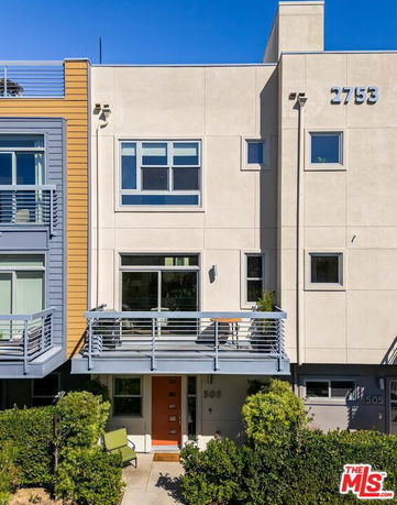 Front view of a modern multi-story building with large windows and a balcony.