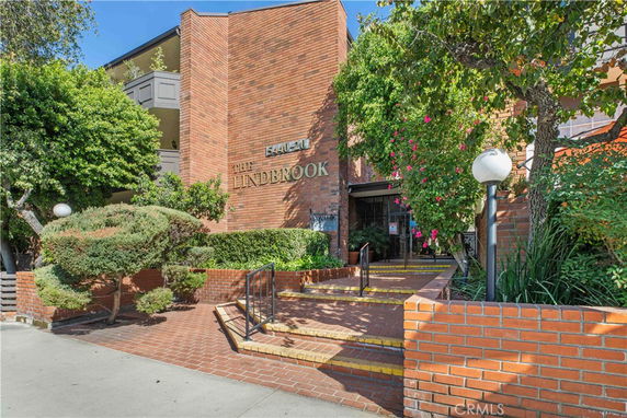 Front view of a brick building entrance with stairs and greenery.