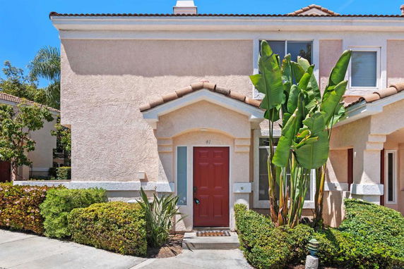 Front view of a two-story house with a red door and surrounding plants.
