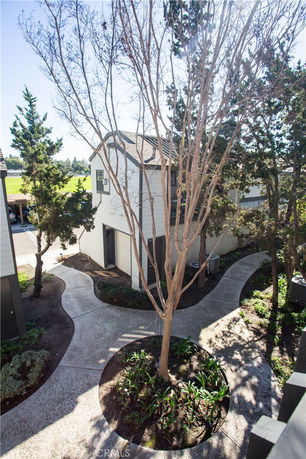 View of a two-story building with white siding and a peaked roof, surrounded by trees and walkways.