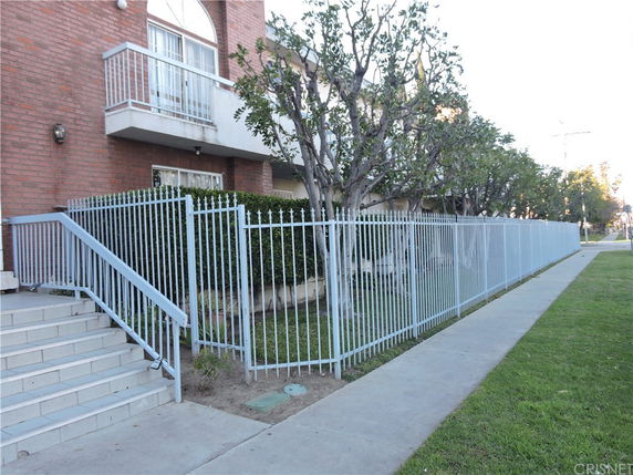 Front view of a building with stairs leading to the entrance, surrounded by a metal fence and small trees.