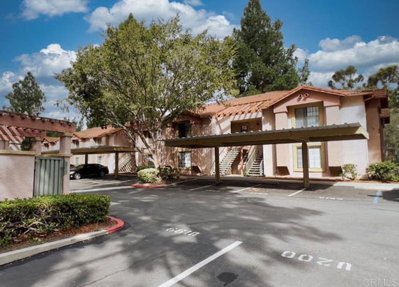 Outdoor parking area in front of a two-story building with a tree nearby.