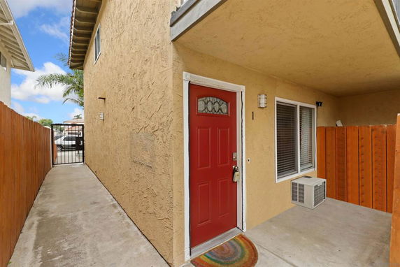 Front view of a two-story house with a red door and a small patio area.
