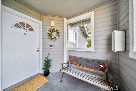Front porch area with a light gray painted wall, decorative bench, and a white door with a wreath.