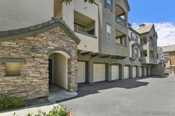 Front view of a multi-story residential building with stone and stucco exterior, including multiple garages.