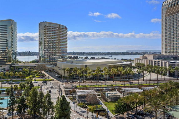 View of multiple large buildings and palm trees with a waterfront in the background.