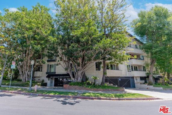 Front view of a multi-story residential building with balconies and surrounded by trees.