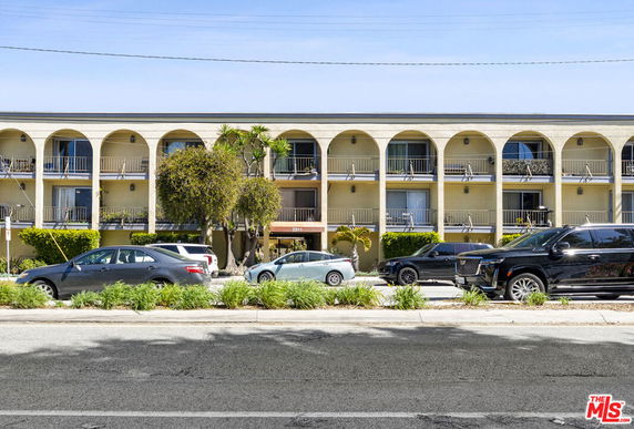 Front view of a multi-story building with arched balconies and several parked cars.