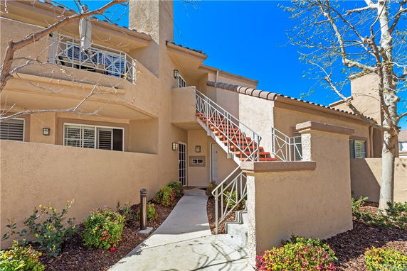 Front view of a two-story beige stucco house with external staircase and balcony.