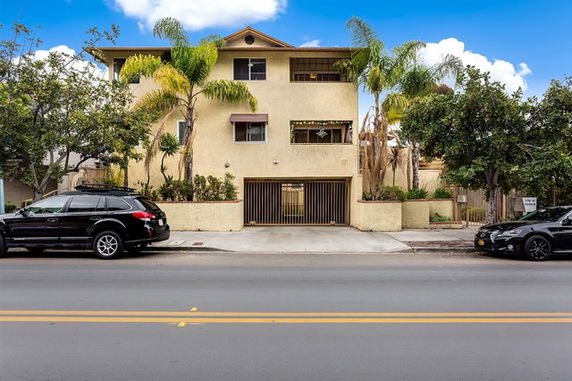 Front view of a three-story residential building with a gated entrance and palm trees.