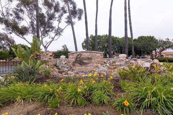 Outdoor view featuring a landscaped area with a stone sign and tall palm trees.