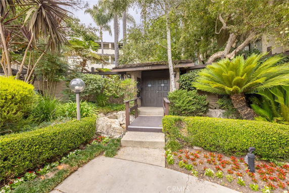 Front view of a house with a wooden door and surrounded by lush greenery.