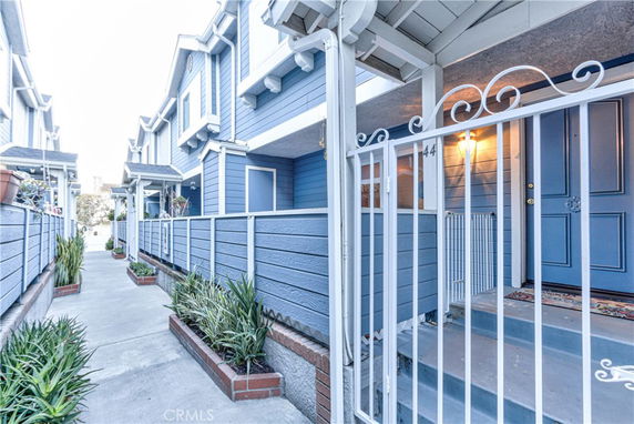 Front view of a modern townhouse with blue siding and white trim, featuring covered entryways and gated porches.