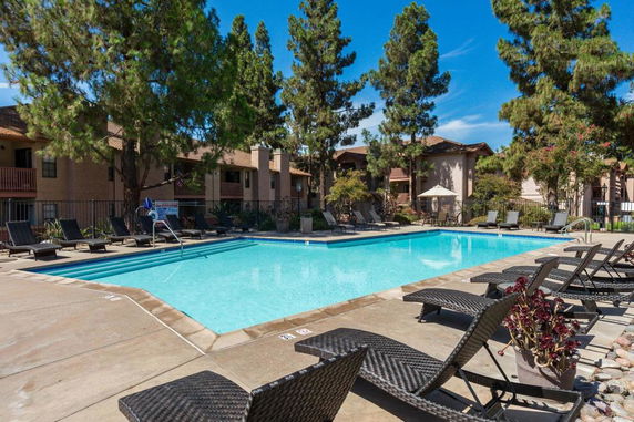 Swimming pool area surrounded by lounge chairs and trees.