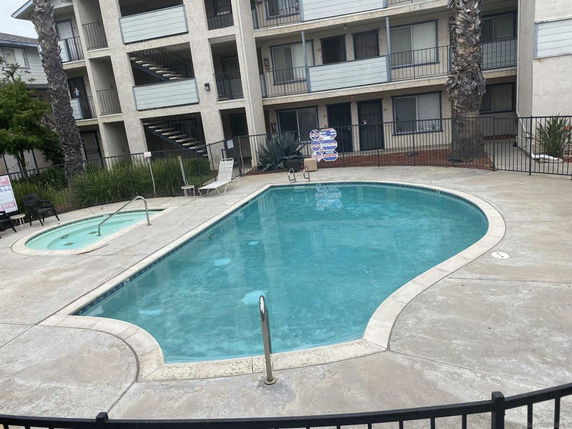 Outdoor swimming pool area in front of a multi-story residential building.
