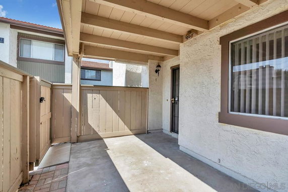 Front view of an apartment entrance with a covered walkway and wooden fencing.