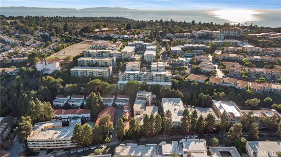 Aerial view of a residential area with multiple apartment buildings surrounded by greenery and a view of the sea in the background.