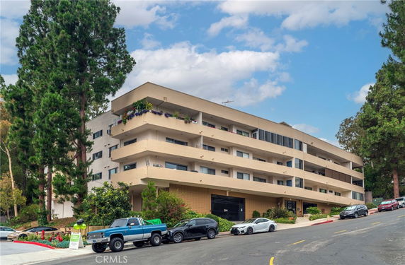 Front view of a multi-story building with balconies and surrounding trees.