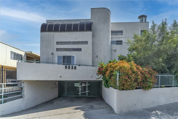 Front view of a multi-story building with a gated entrance and plants.
