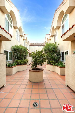 Courtyard view between two residential buildings with plants and tiled flooring.